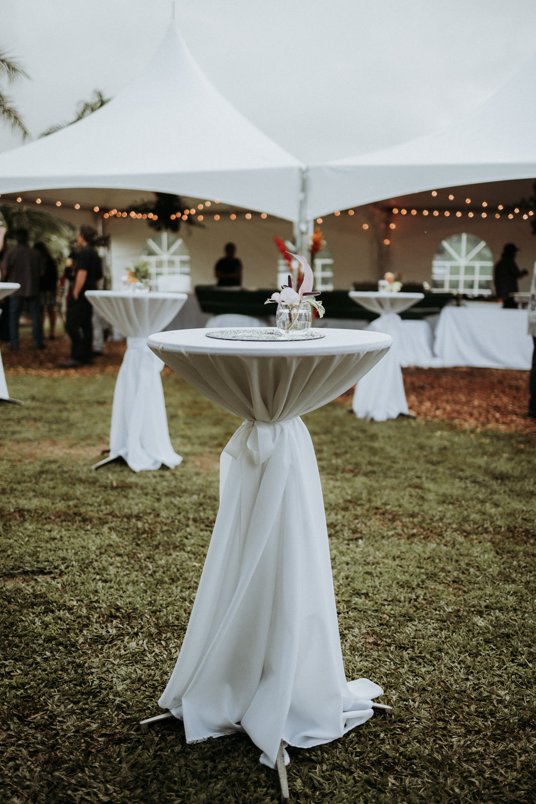 wedding tent in the background and cocktail tables draped in white linens